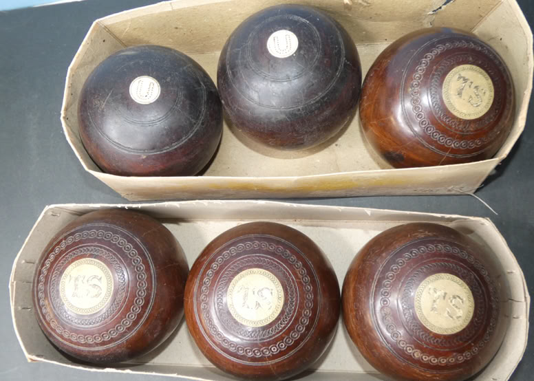 Two boxes containing sets of dark-colored lawn bowls with circular markings on top.